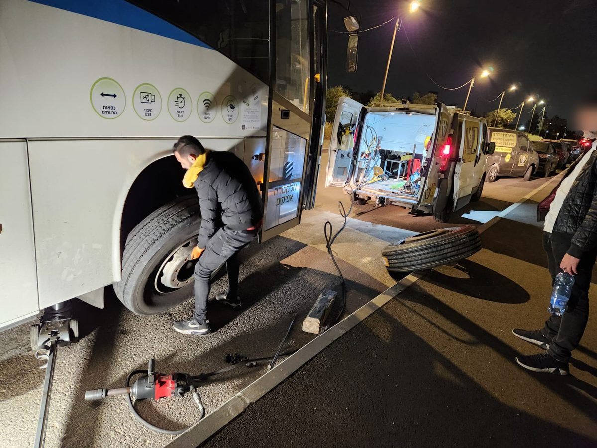 טכנאי פנדה מחליף גלגל לאוטובוס בלילה, וניידת השירות פתוחה מאחור