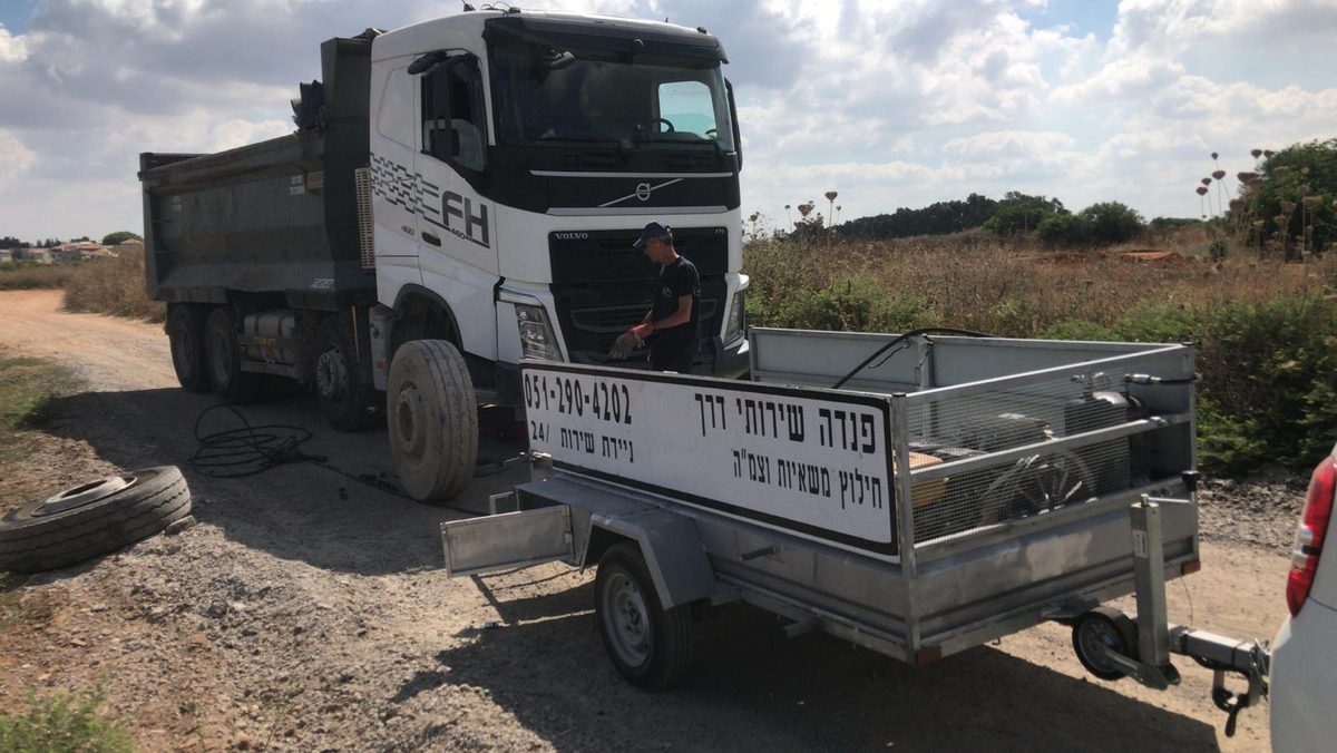 טכנאי פנדה מחליף גלגל למשאית רכינה בשטח פתוח, ליד נגרר השירות של פנדה
